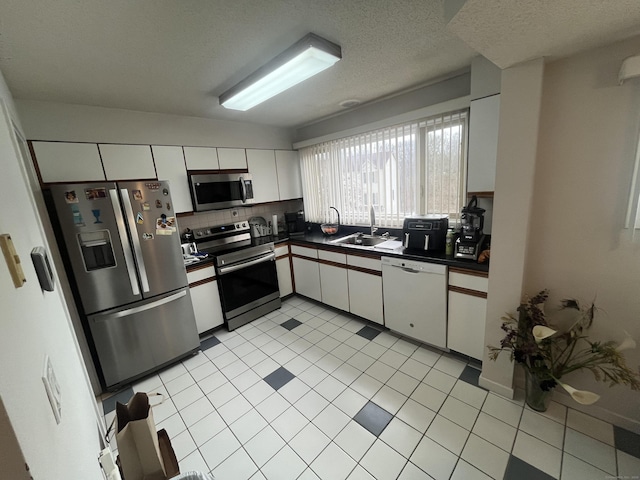 kitchen featuring tasteful backsplash, white cabinets, dark countertops, appliances with stainless steel finishes, and a sink