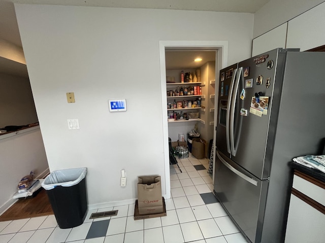 kitchen with light tile patterned floors, stainless steel refrigerator with ice dispenser, visible vents, and white cabinets