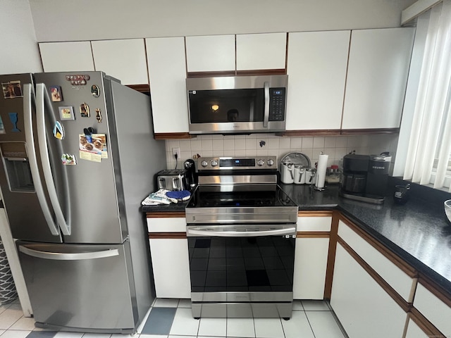 kitchen featuring light tile patterned flooring, white cabinets, appliances with stainless steel finishes, decorative backsplash, and dark countertops