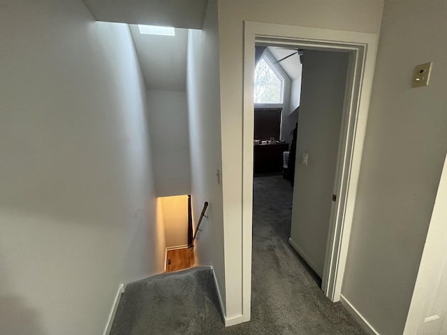 hall with baseboards, dark carpet, and an upstairs landing