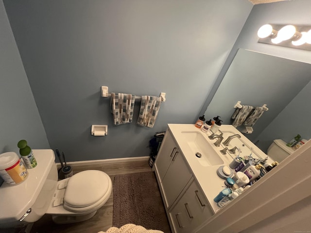 half bath featuring toilet, baseboards, wood finished floors, and vanity