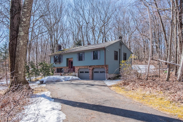 raised ranch featuring a garage, a chimney, aphalt driveway, and brick siding