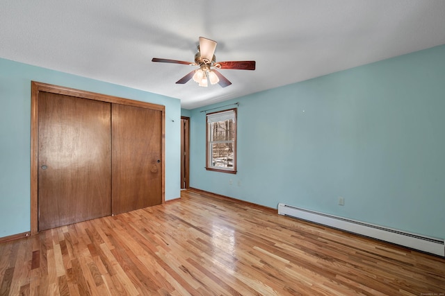 unfurnished bedroom featuring light wood finished floors, baseboard heating, a closet, and baseboards