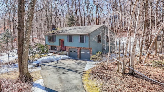 bi-level home featuring driveway, brick siding, a chimney, and an attached garage