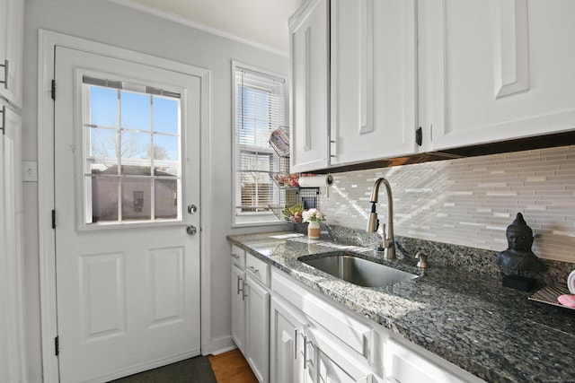 kitchen featuring crown molding, decorative backsplash, white cabinets, a sink, and dark stone counters