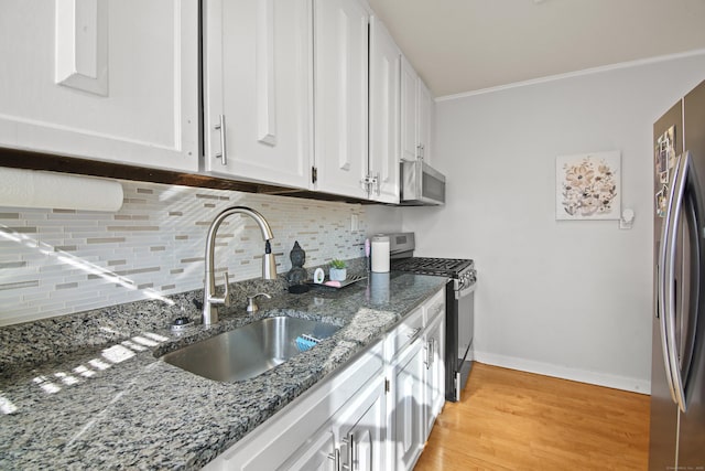 kitchen featuring light wood finished floors, white cabinets, a sink, stainless steel appliances, and backsplash