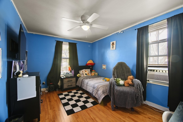 bedroom with ornamental molding, cooling unit, wood-type flooring, and a ceiling fan