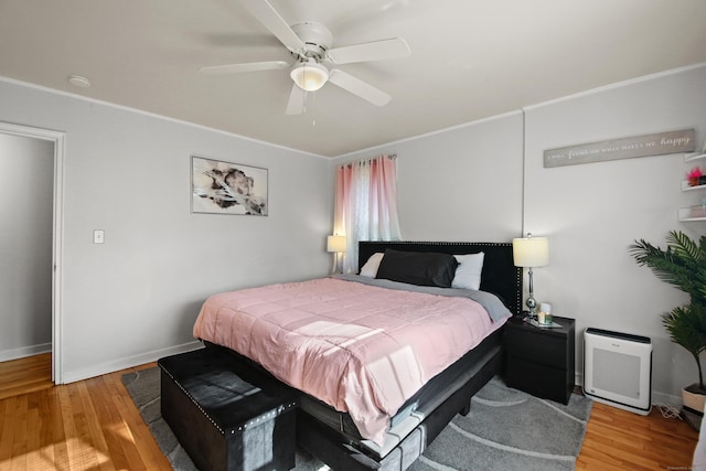 bedroom with a ceiling fan, crown molding, baseboards, and wood finished floors