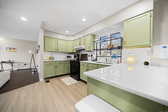 kitchen with black electric range oven, a sink, light wood-style floors, green cabinets, and white microwave