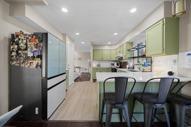 kitchen featuring freestanding refrigerator, a peninsula, green cabinets, and a sink