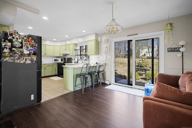 kitchen featuring white microwave, green cabinets, a breakfast bar area, a peninsula, and freestanding refrigerator