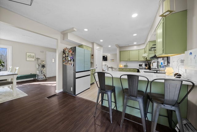 kitchen with wood finished floors, green cabinetry, a peninsula, freestanding refrigerator, and a sink