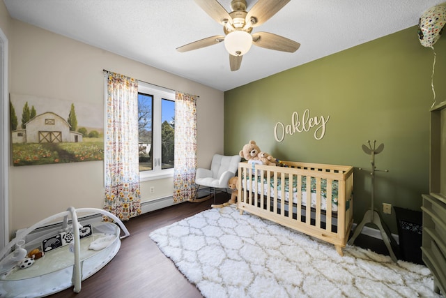 bedroom with a crib, a textured ceiling, wood finished floors, and a ceiling fan