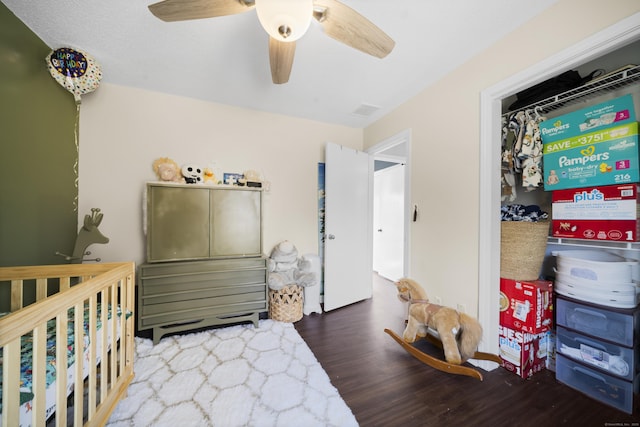 bedroom with visible vents, a nursery area, wood finished floors, and a ceiling fan