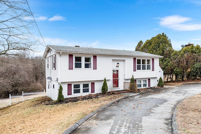 bi-level home with a shingled roof and fence