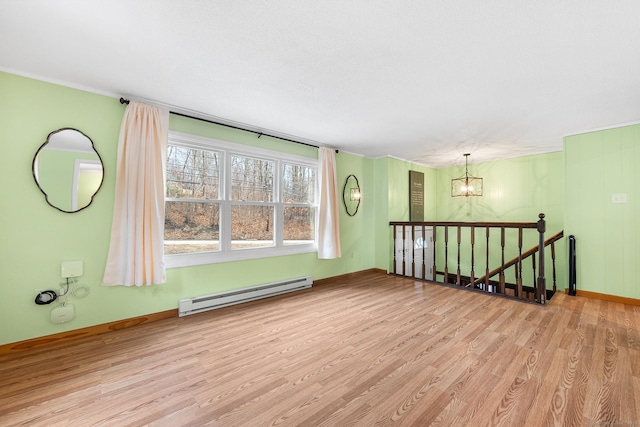 empty room featuring a baseboard radiator, a notable chandelier, baseboards, and wood finished floors