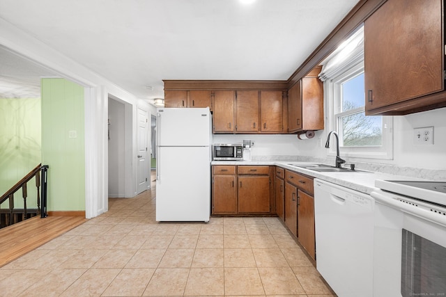 kitchen with light tile patterned floors, light countertops, brown cabinetry, a sink, and white appliances