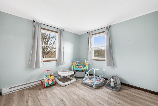 recreation room featuring a baseboard heating unit, plenty of natural light, baseboards, and wood finished floors