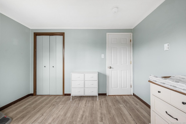 unfurnished bedroom featuring light wood-style floors, baseboards, a closet, and ornamental molding