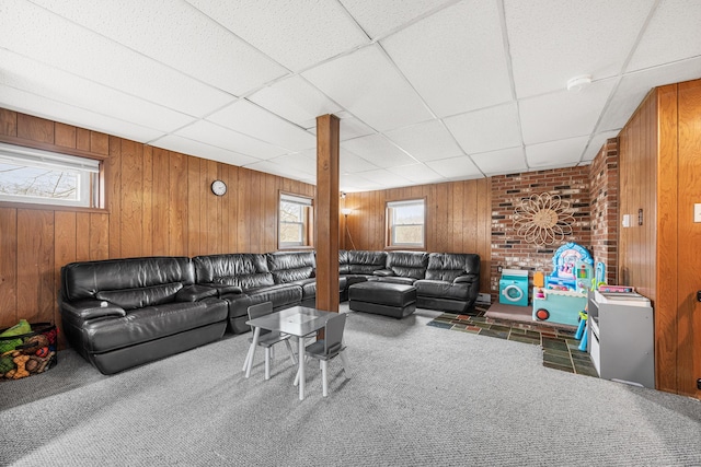 carpeted living area featuring wood walls and a drop ceiling