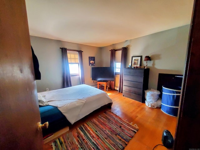 bedroom with a baseboard heating unit and wood finished floors