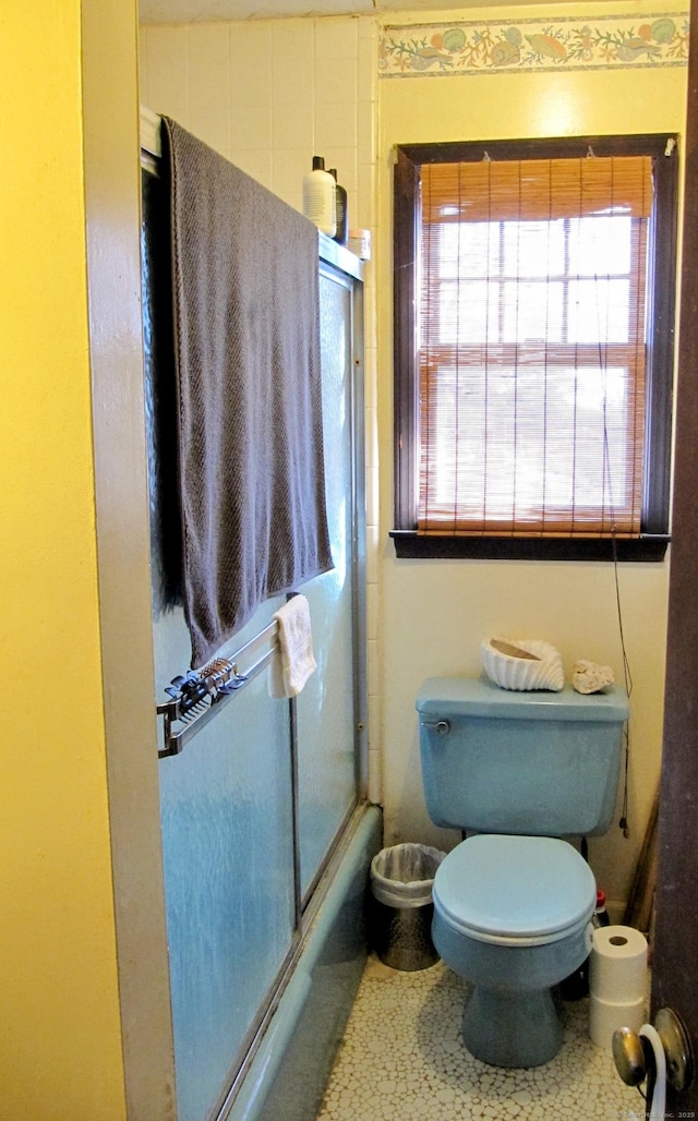 full bath featuring toilet and bath / shower combo with glass door