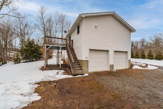 view of snow covered exterior with driveway, stairway, an attached garage, and a wooden deck