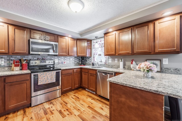 kitchen featuring stainless steel appliances, brown cabinetry, light wood-style floors, a sink, and a peninsula