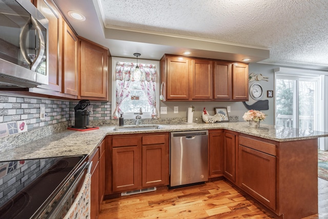 kitchen featuring stainless steel appliances, brown cabinetry, a peninsula, and light wood-style flooring