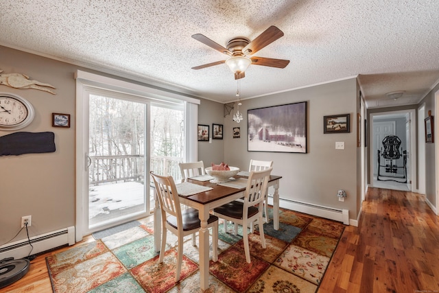 dining area with a textured ceiling, ornamental molding, a baseboard radiator, and wood finished floors