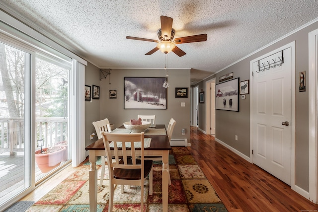 dining space featuring a textured ceiling, a baseboard heating unit, wood finished floors, and ornamental molding