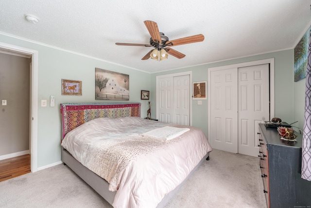 carpeted bedroom featuring multiple closets, crown molding, a textured ceiling, and a ceiling fan