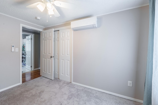 unfurnished bedroom with carpet, a textured ceiling, crown molding, a closet, and a wall mounted AC