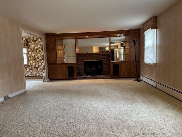 unfurnished living room with baseboard heating, a brick fireplace, and carpet floors