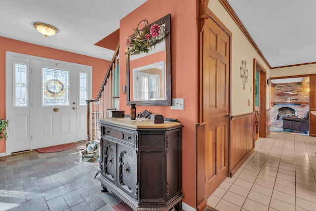 entryway featuring stairs, stone finish floor, a fireplace, and ornamental molding