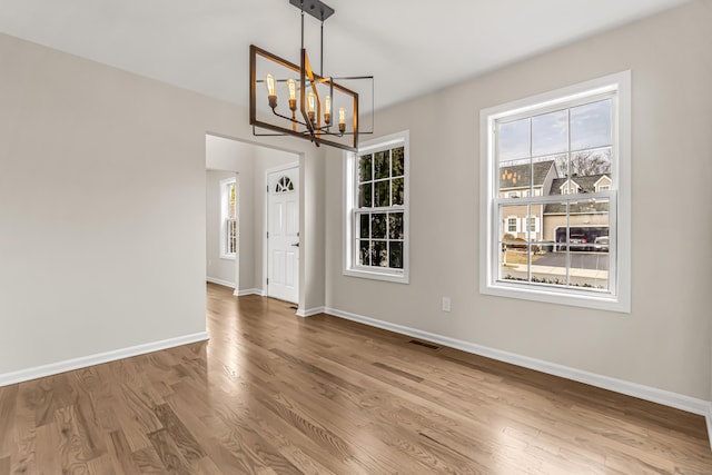 unfurnished dining area with a chandelier, visible vents, baseboards, and wood finished floors