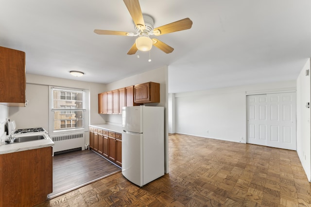 kitchen with radiator heating unit, light countertops, freestanding refrigerator, brown cabinetry, and a sink