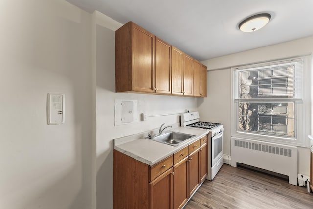 kitchen with light wood-style flooring, gas range gas stove, radiator heating unit, a sink, and light countertops