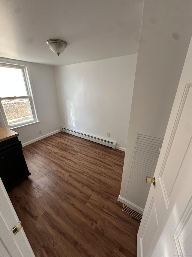 unfurnished room featuring dark wood-type flooring, baseboards, and a baseboard radiator