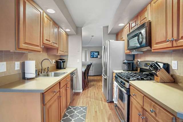 kitchen featuring light wood finished floors, tasteful backsplash, appliances with stainless steel finishes, light countertops, and a sink