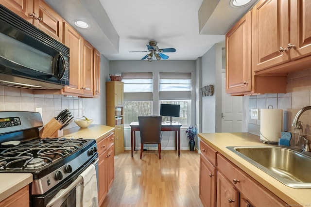 kitchen featuring black microwave, light wood-style flooring, a sink, light countertops, and stainless steel gas range