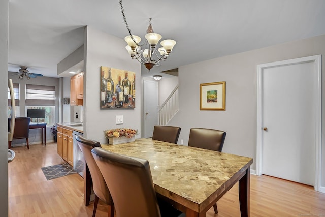 dining space featuring ceiling fan with notable chandelier, light wood-style flooring, baseboards, and stairs