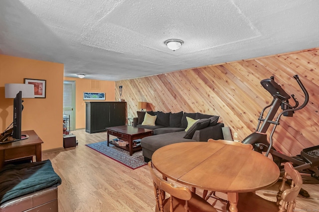 living room with light wood-type flooring, wood walls, and a textured ceiling