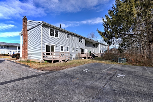 back of house with a deck, uncovered parking, and a chimney