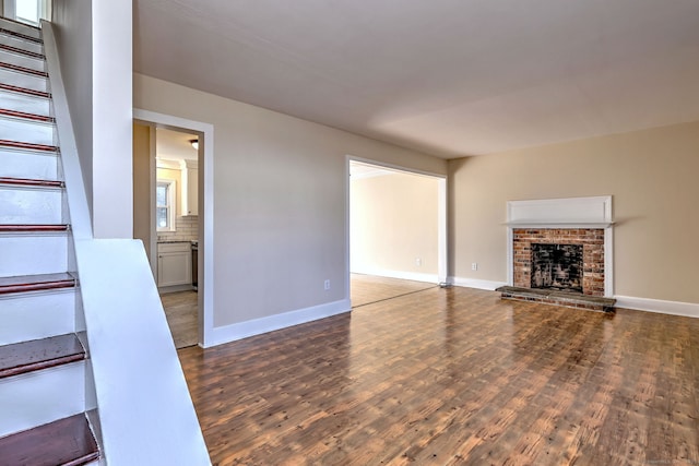 unfurnished living room with stairway, a fireplace, baseboards, and wood finished floors