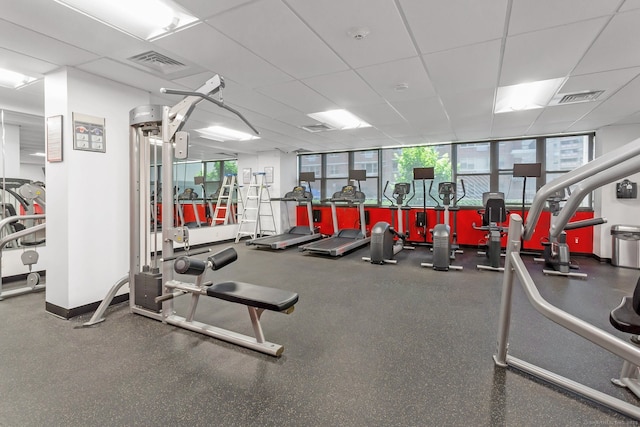 exercise room with a paneled ceiling, visible vents, and baseboards