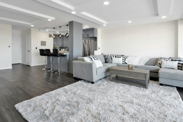 living area with baseboards, a raised ceiling, dark wood-style flooring, and recessed lighting