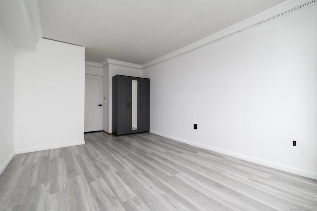 empty room with baseboards, light wood-type flooring, and crown molding