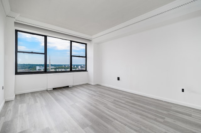 spare room featuring ornamental molding, baseboards, radiator heating unit, and wood finished floors