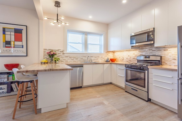 kitchen with butcher block counters, appliances with stainless steel finishes, white cabinetry, a sink, and a kitchen breakfast bar